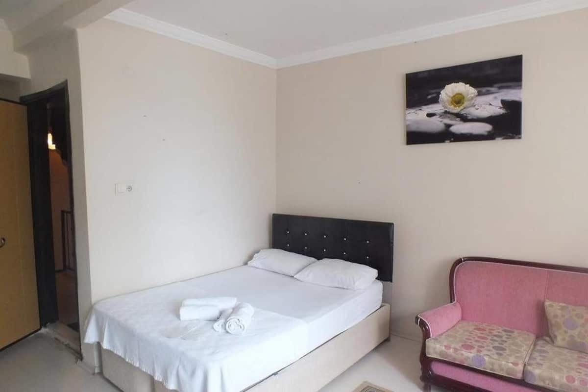 A bedroom with a bed, a pink sofa, and a painting of a flower on the wall.