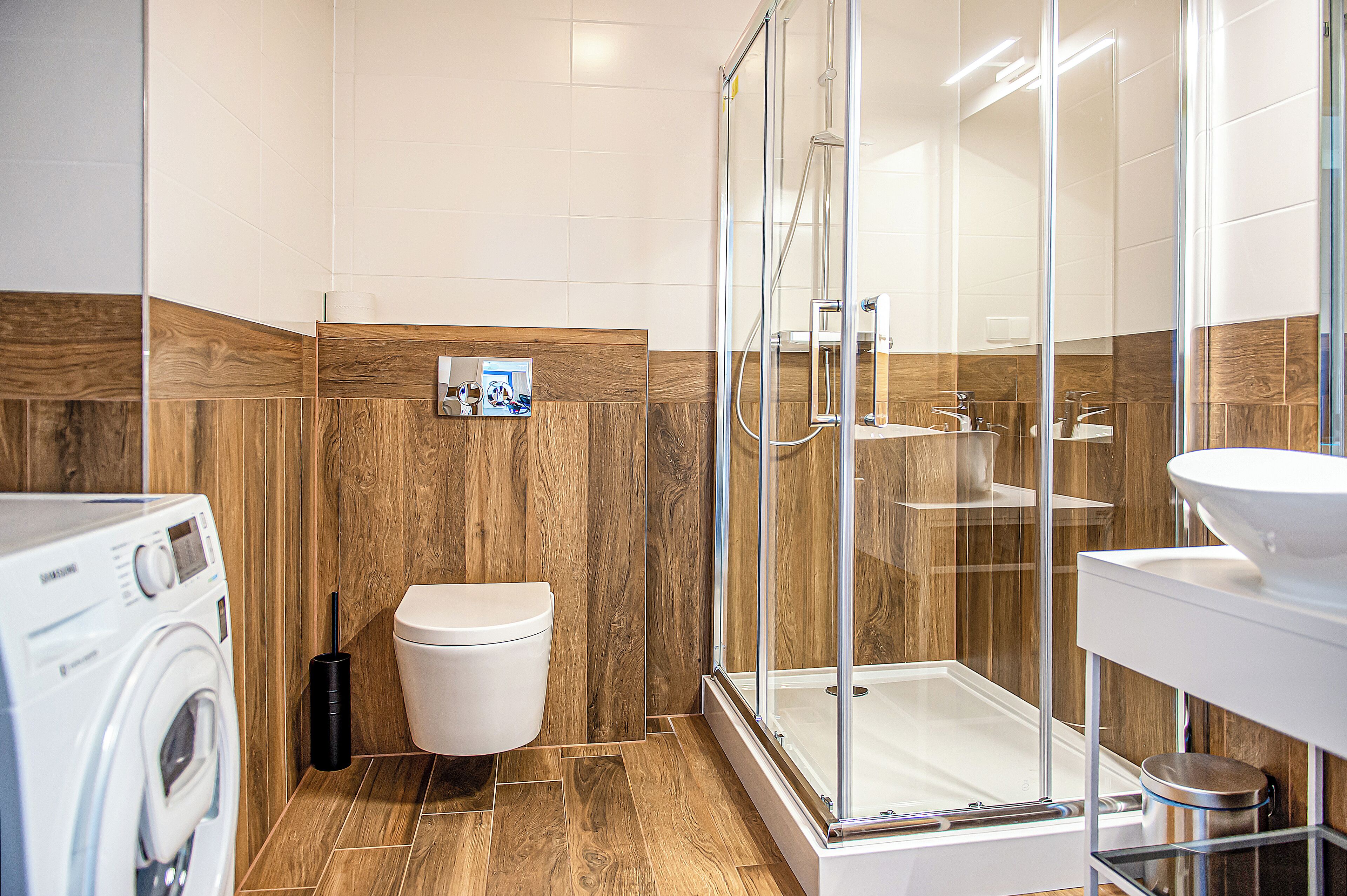 Ein modernes Badezimmer mit einer Glaskabine zur Dusche, einer weißen Toilette und einer Waschmaschine.