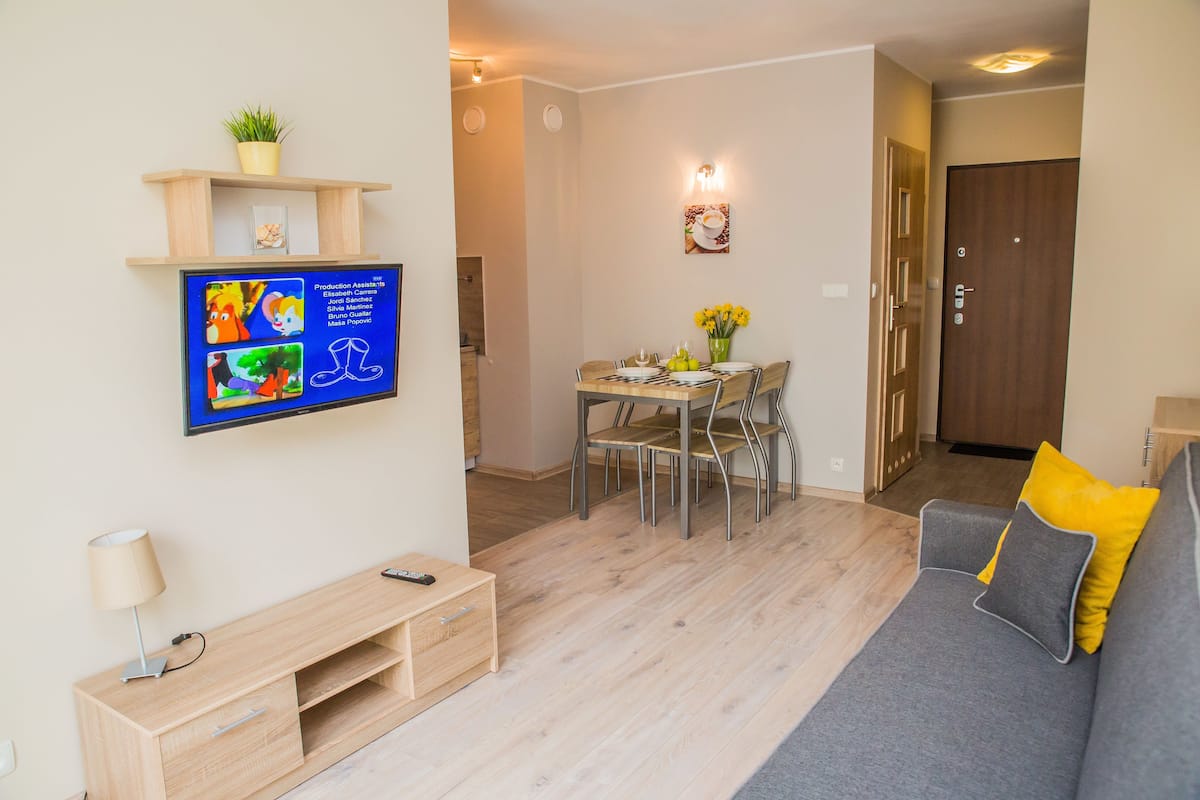 Ein modernes Wohnzimmer mit grauem Sofa, einem Holz-Entertainment-System und einem Essbereich mit Tisch und Stühlen.