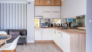 Eine kleine Küche mit weißen Schränken, einer Holz Arbeitsplatte und einem Essbereich mit grauem Sofa und weißen Stühlen.