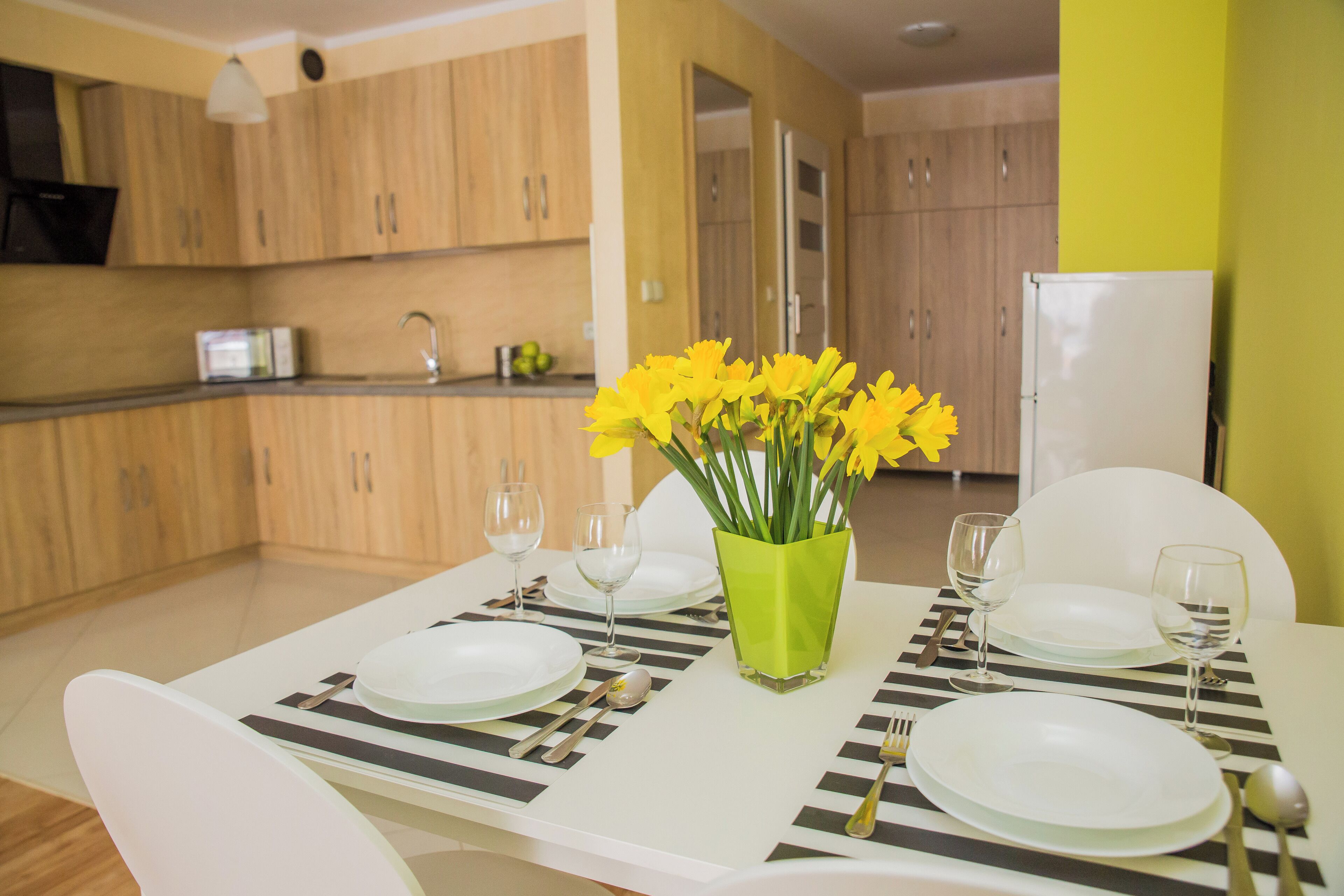 A dining table set with plates, cutlery, and glasses, with a vase of yellow flowers in the center.