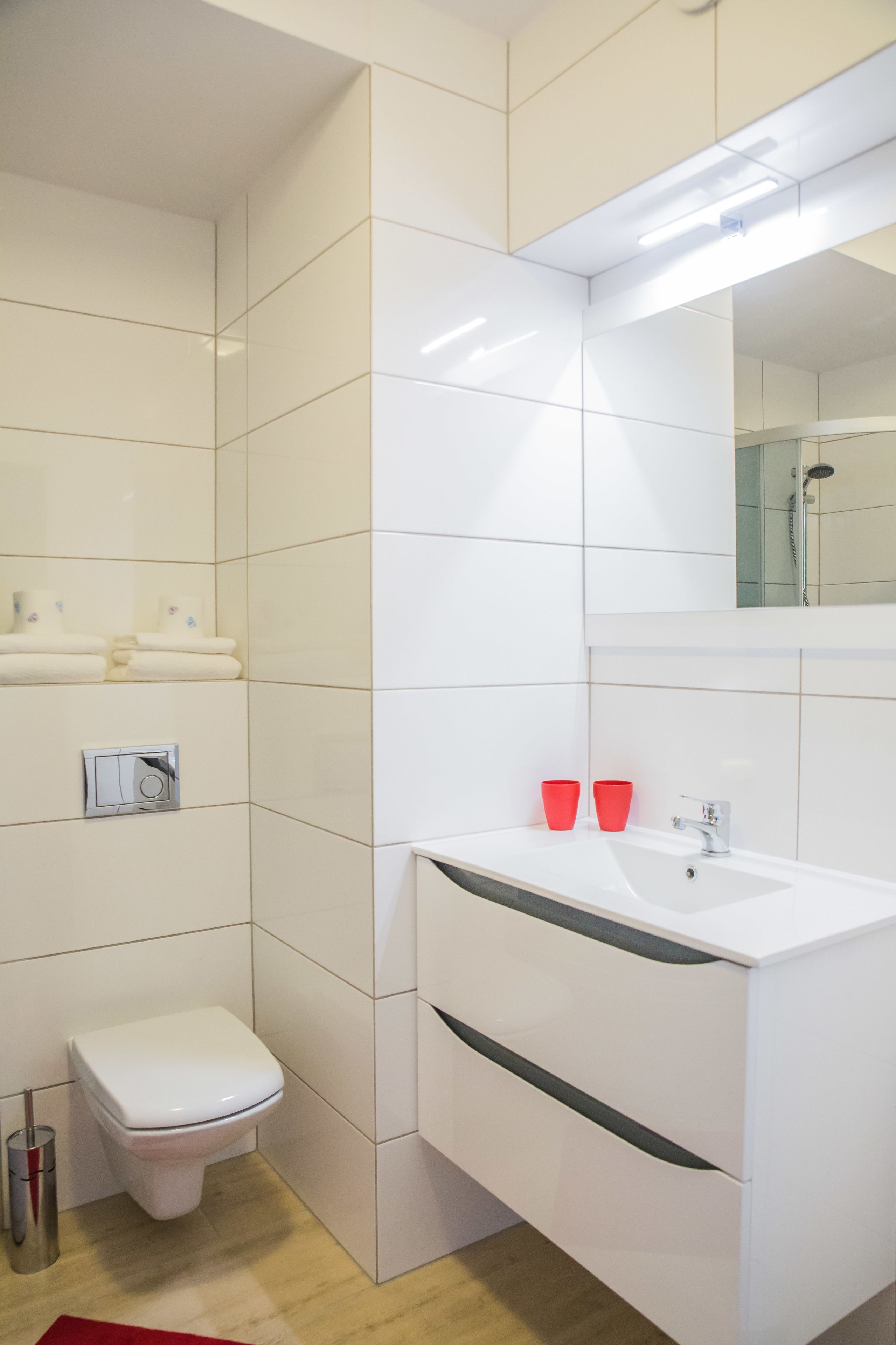 A modern bathroom with white tiles, a white sink, a mirror, and a shower.