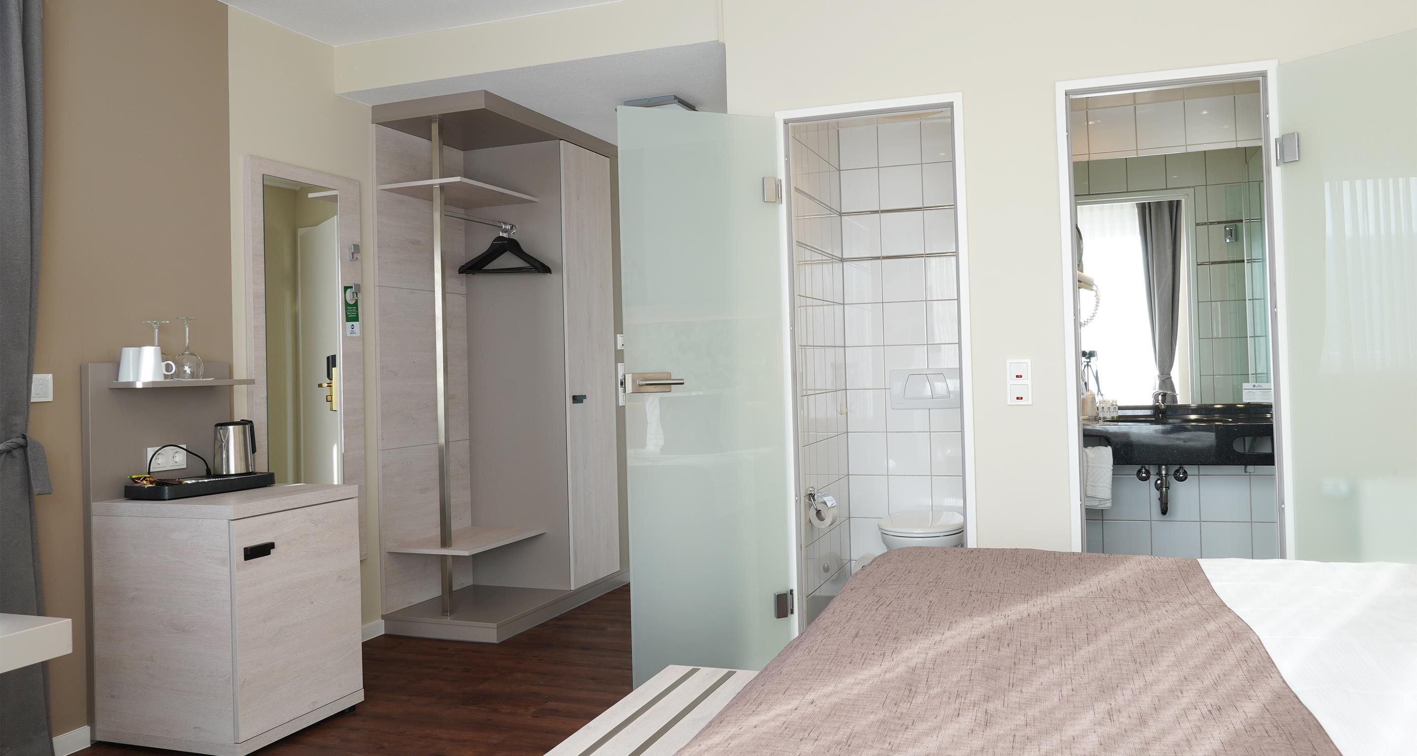 Ein Hotelzimmer mit Bett, Nachttisch, Schrank, Duschbereich und Badezimmer inklusive Waschbecken und Spiegel.