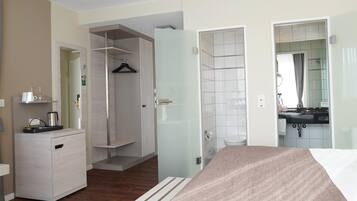 Ein Hotelzimmer mit Bett, Nachttisch, Schrank, Duschbereich und Badezimmer inklusive Waschbecken und Spiegel.