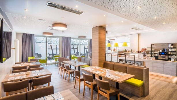A modern restaurant with wooden tables and chairs, a bar area, and a view of the city.
