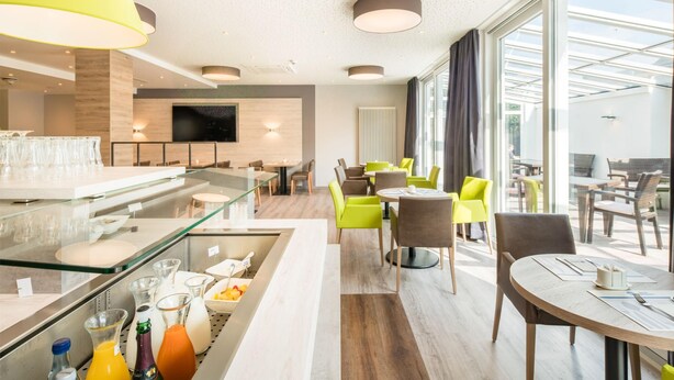 A modern hotel room with a dining area, a kitchen, and a large window offering a view. - Best Western Hotel St. Michael (Morbach)