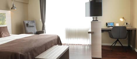 A hotel room with a bed, a desk with a computer, a chair, and a television.