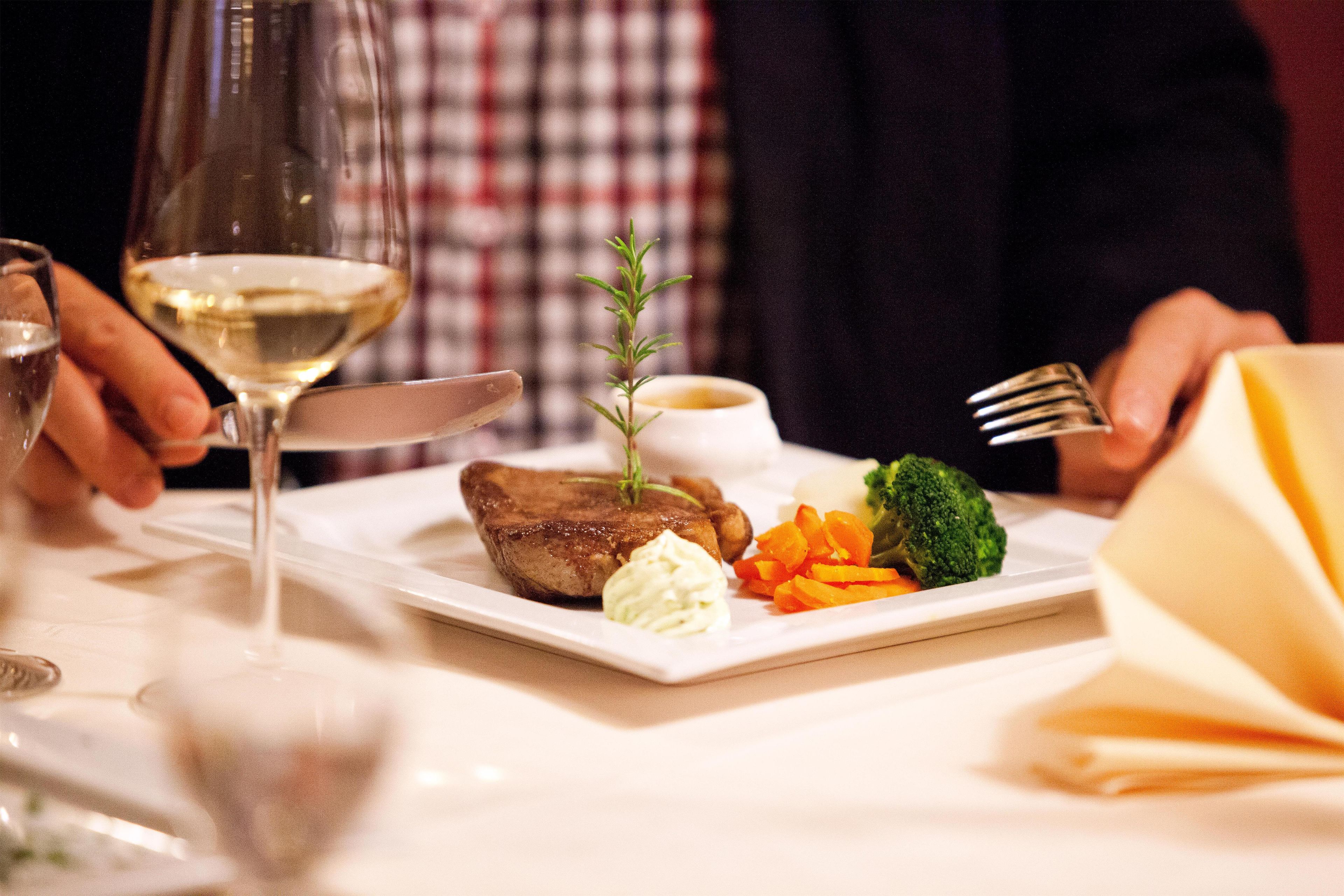 A dining table with a plate of food, a glass of white wine, and a fork.