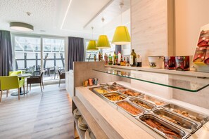 A buffet area with various food options, a seating area with chairs, and a view of the outdoors. - Best Western Hotel St. Michael (Morbach)