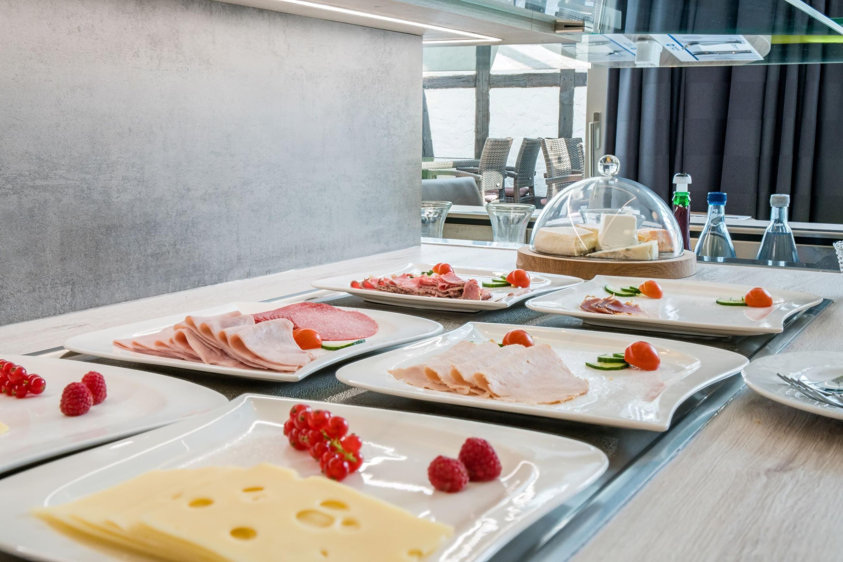 A buffet with various cold cuts, cheeses, and garnishes.