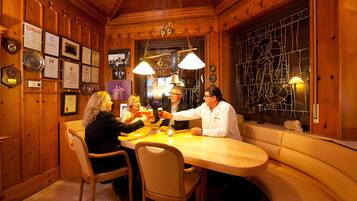Un interior de madera con una mesa de comedor, sillas, diplomas enmarcados y un ventanal de vidrio emplomado.
