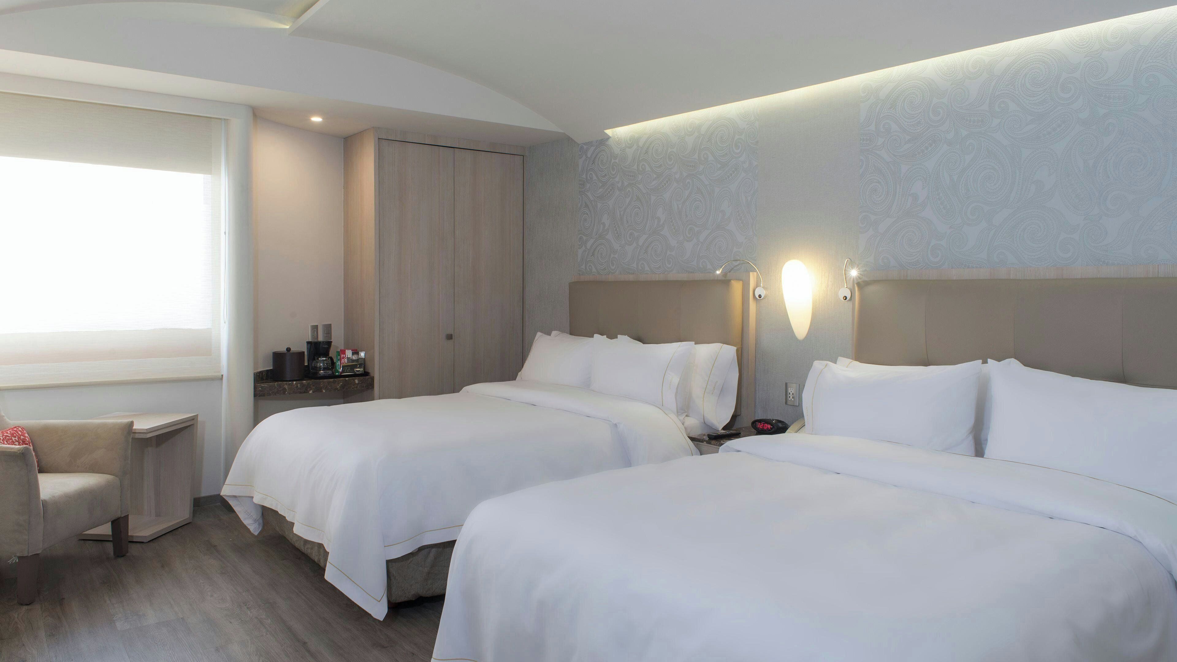 A hotel room with two beds, a seating area, a minibar, and a large window.