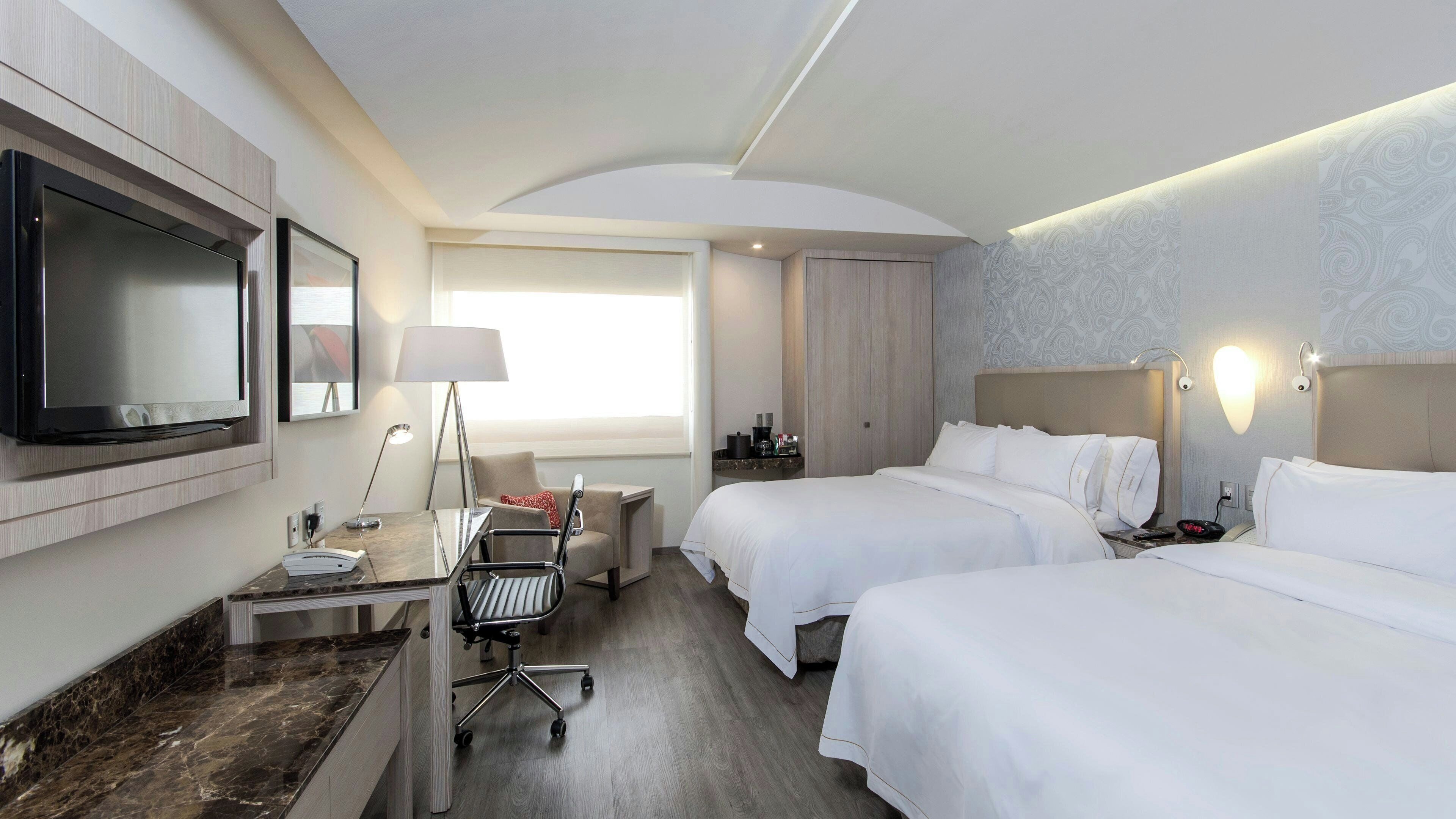 A hotel room with two beds, a desk with a flat-screen TV, a lamp, and a chair.