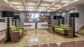 A hotel lobby with a reception desk, two green armchairs, a coffee table, and a large TV screen. - Holiday Inn Express Mexico - Toreo by IHG (Naucalpan)