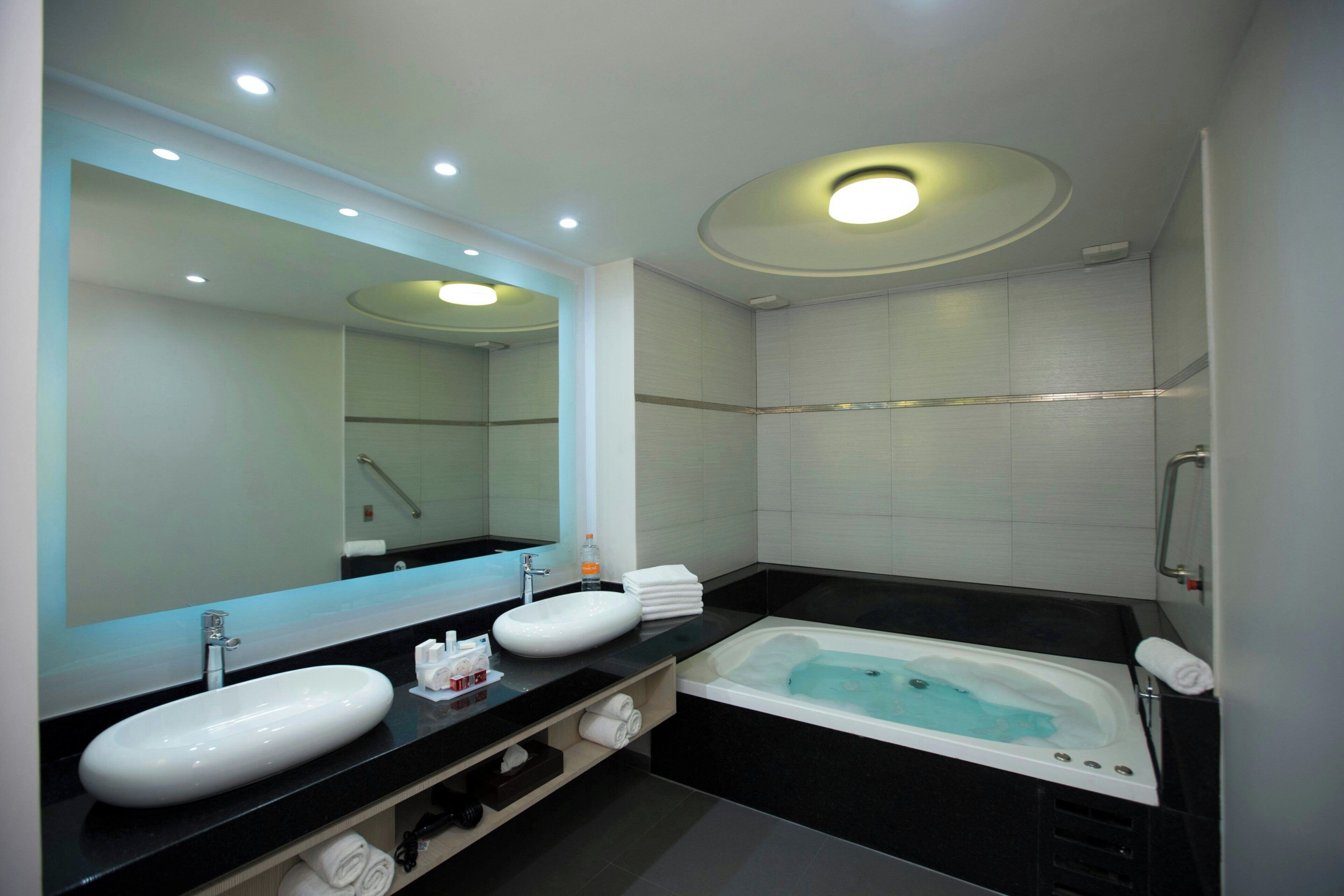 Un baño moderno con un espejo grande, dos lavamanos, una bañera y una ducha.