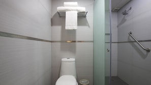 Un baño moderno con inodoro, cabina de ducha de vidrio y barra de apoyo.