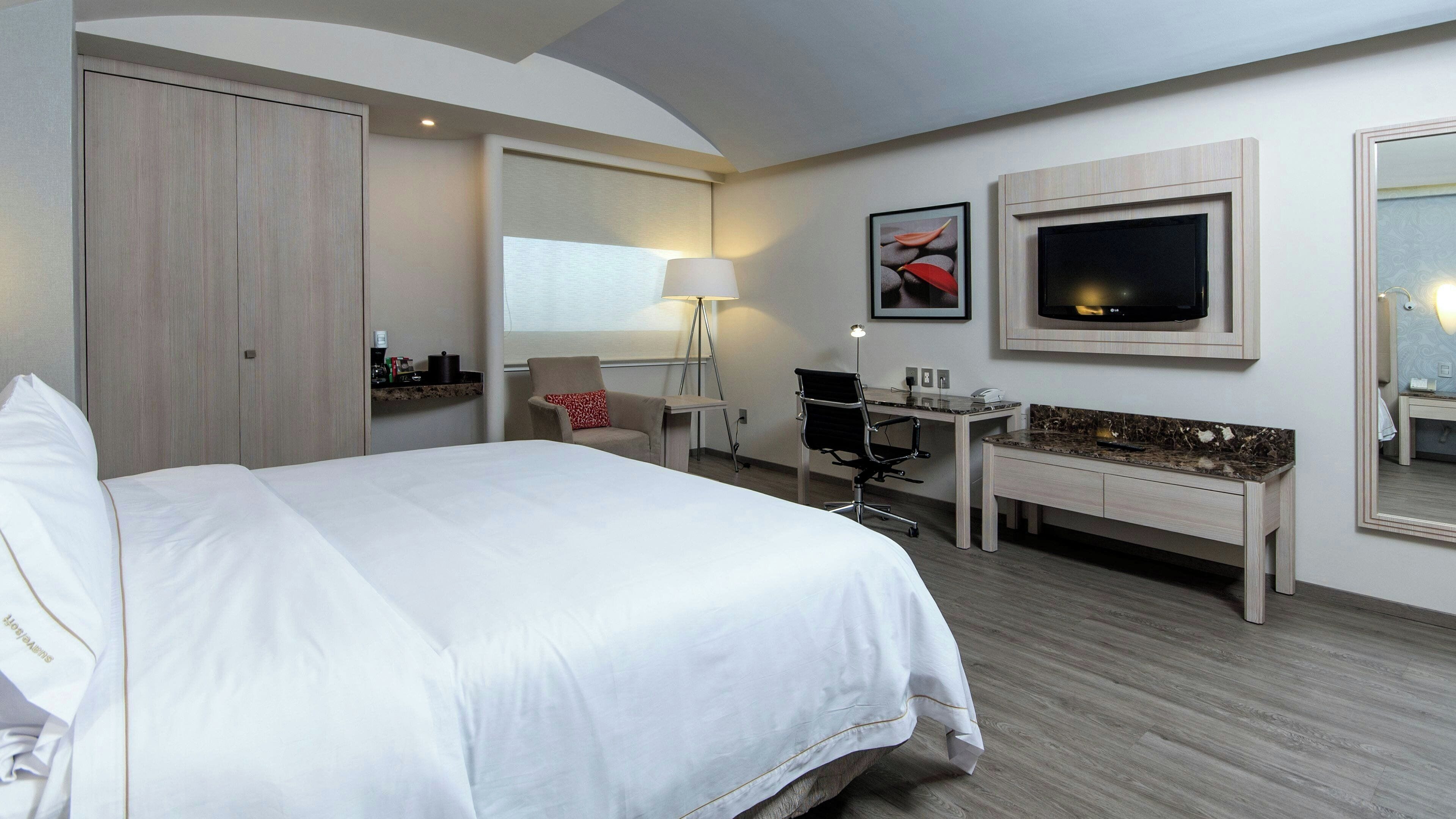 A hotel room with a bed, desk, chair, TV, and a mirror.