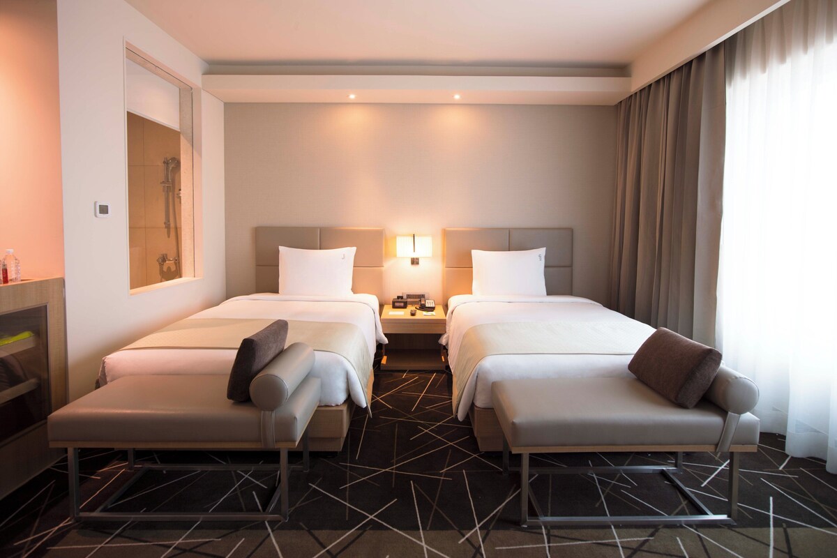 Une chambre d’hôtel avec deux lits, une table de chevet avec une lampe, un miroir et un espace douche.