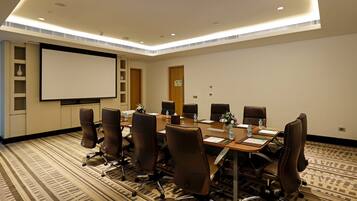 A conference room with a large table, chairs, a projector screen, and a carpeted floor.
