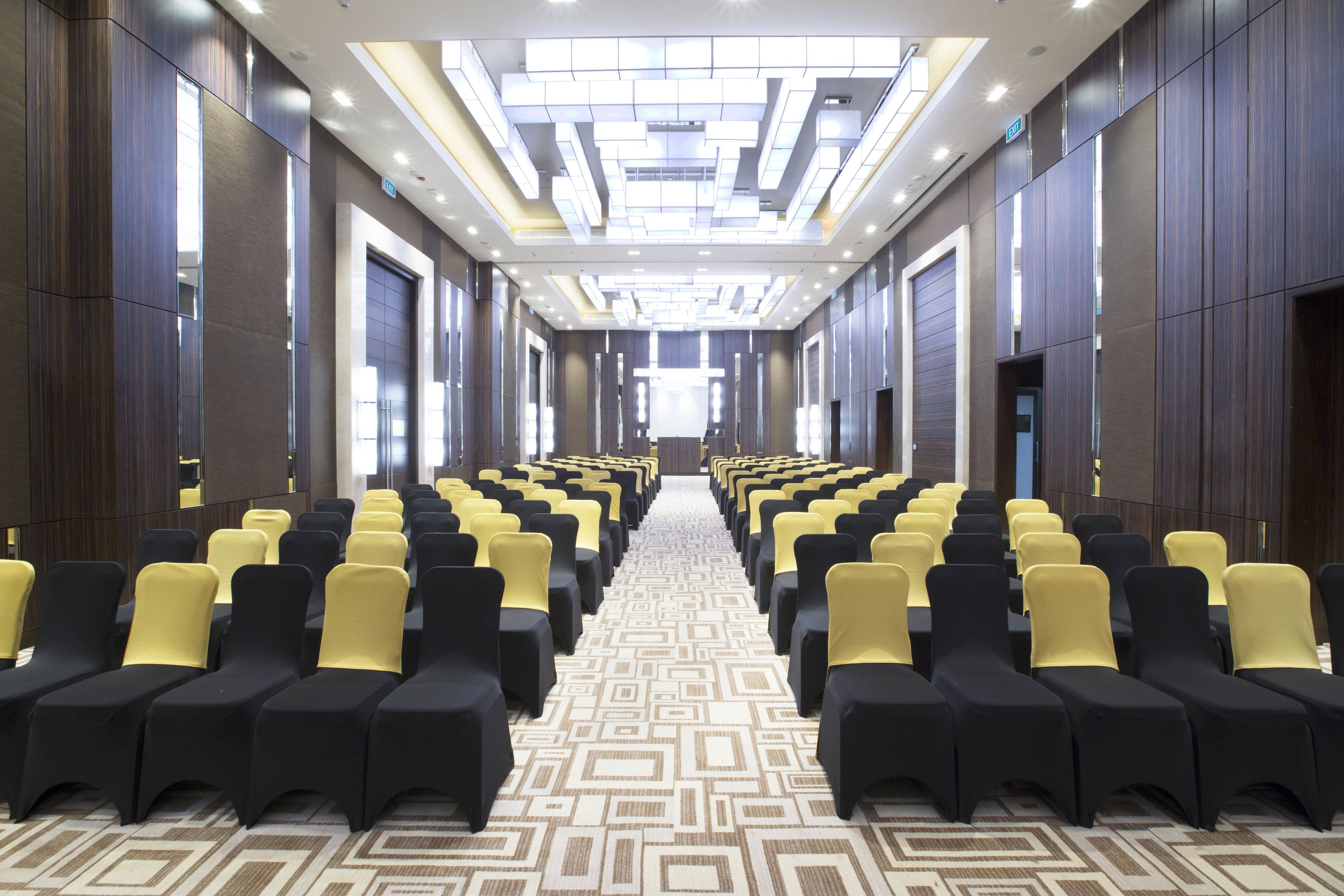 A hotel conference room with rows of chairs, a patterned carpet, and a modern ceiling design.