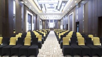 A hotel conference room with rows of chairs, a patterned carpet, and a modern ceiling design.