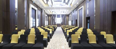 A hotel conference room with rows of chairs, a patterned carpet, and a modern ceiling design.