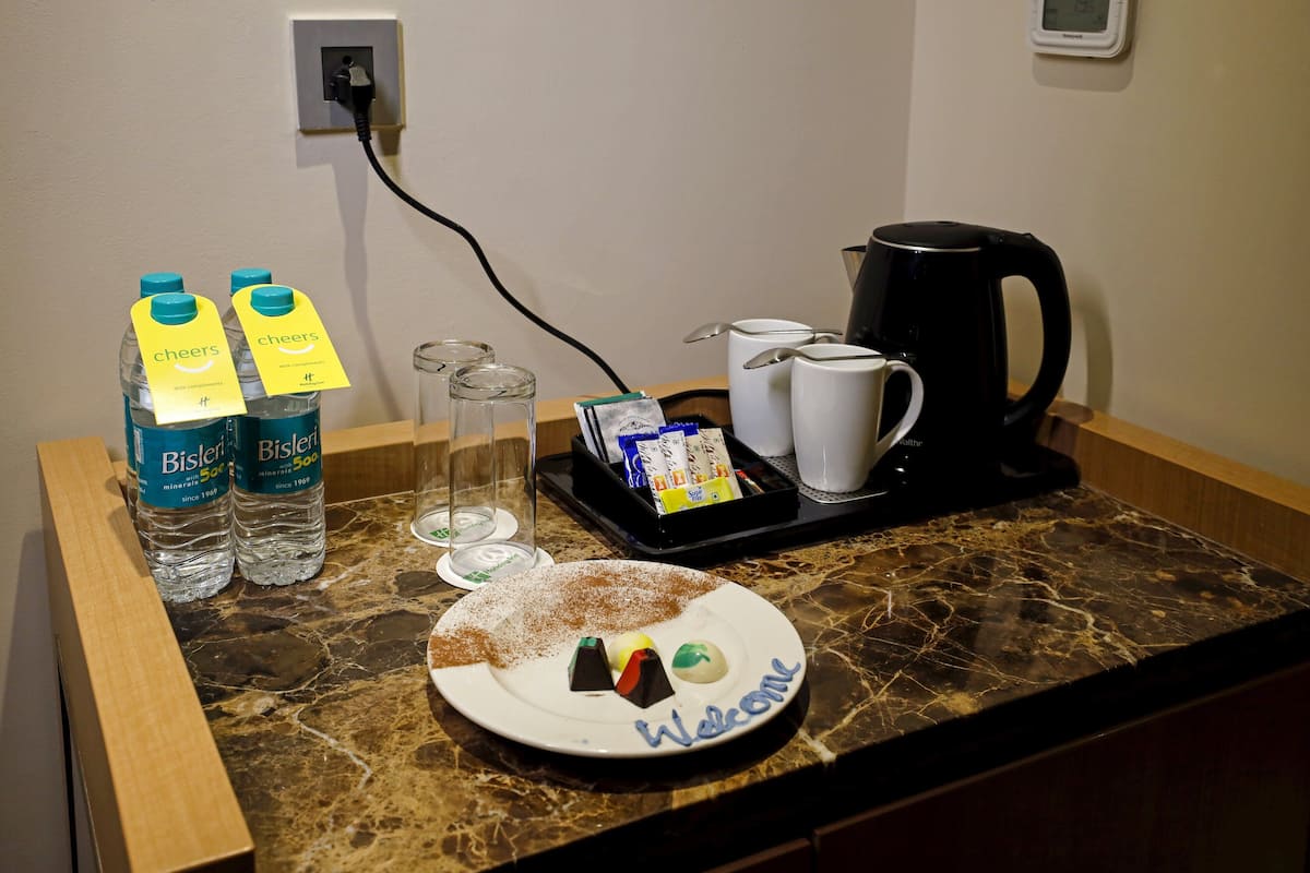 Une table préparée pour le petit-déjeuner avec des bouteilles d’eau Bisleri, une assiette portant un message de bienvenue, des verres, une machine à café et un plateau avec des condiments.