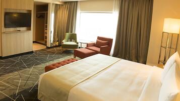 A hotel room with a large bed, a television, a green armchair, a red armchair, and a small table.
