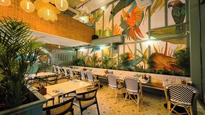 A restaurant interior with a mural of parrots, wicker furniture, and patterned flooring.