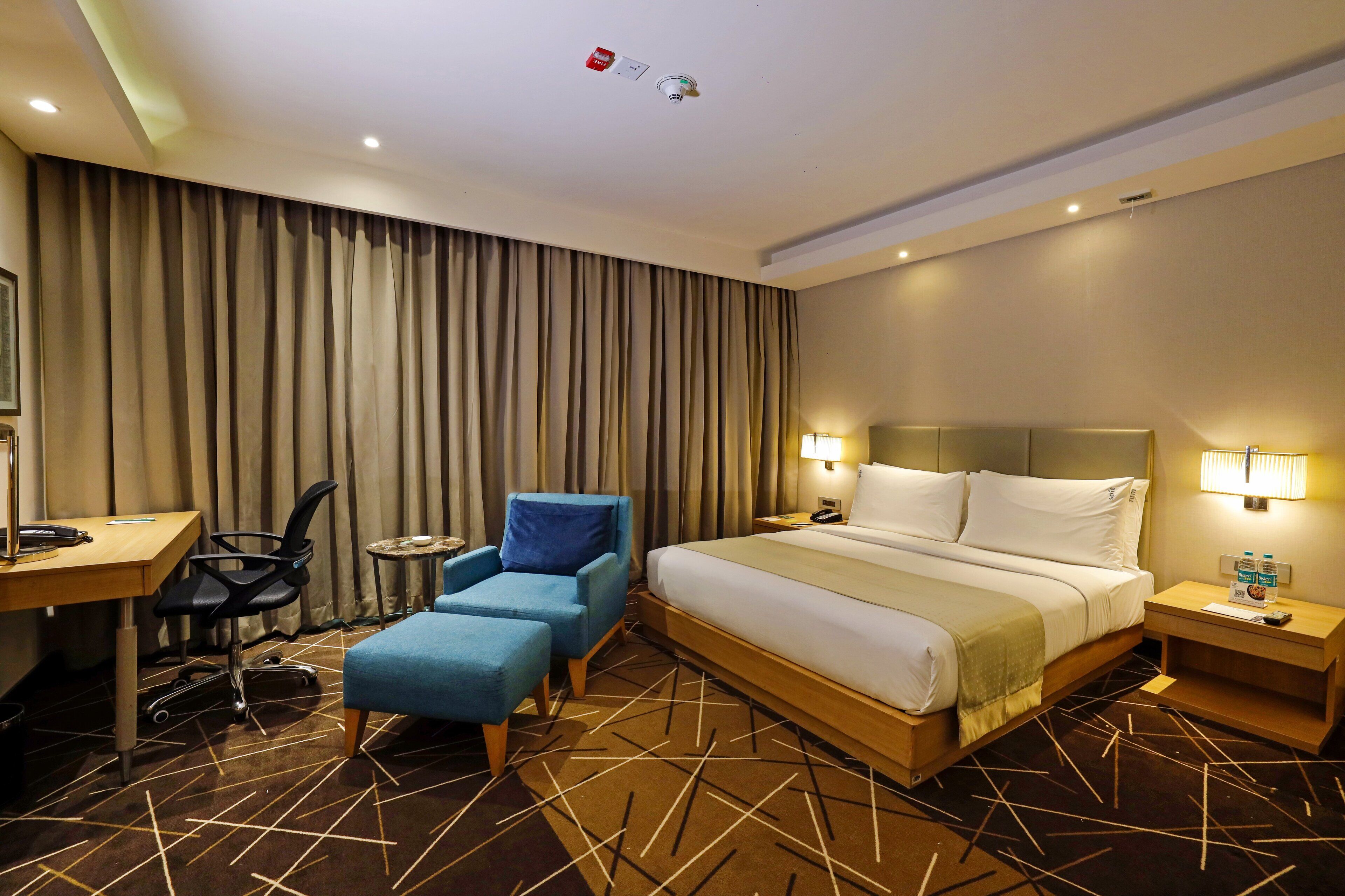 Habitación de hotel con una cama grande, un escritorio con una silla, una mesita pequeña y un sillón azul.
