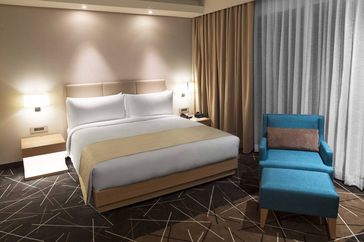 Une chambre d’hôtel moderne avec un grand lit, un fauteuil bleu et une table de chevet avec une lampe.