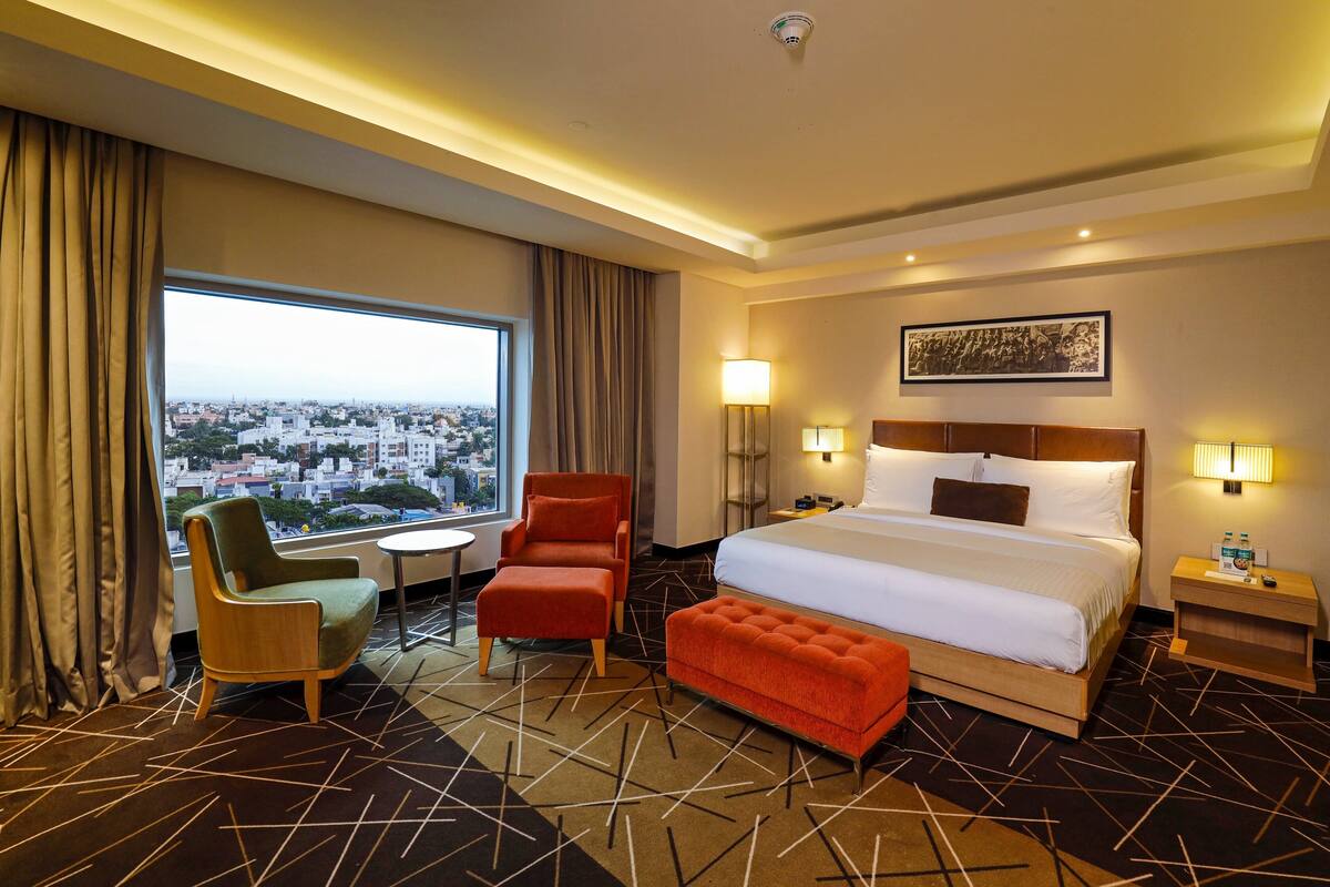 Une chambre d’hôtel avec un grand lit, deux fauteuils, une table ronde et une vue sur le paysage urbain.