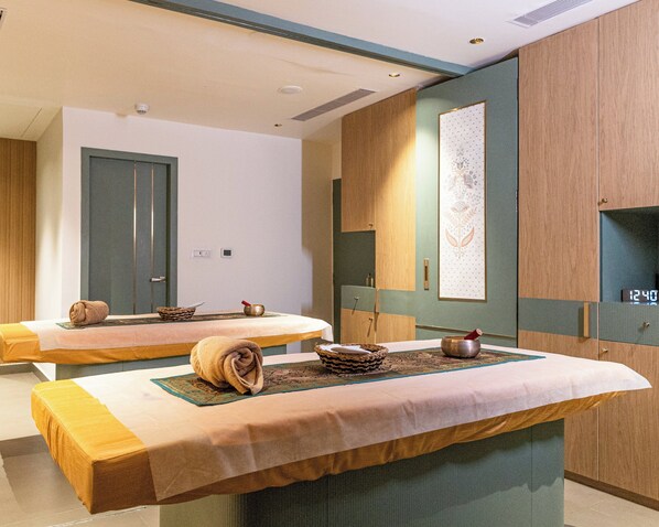 A spa room with two massage tables, a wooden cabinet, a wall-mounted clock, and a decorative panel.