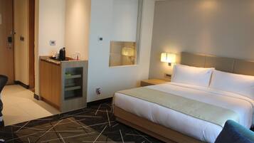 Une chambre d’hôtel comprenant un lit, un bureau, une chaise, un miroir et une table de chevet avec une lampe.