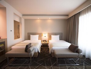 Una habitación de hotel con dos camas, una mesita de noche, un espejo y una ventana con cortinas.