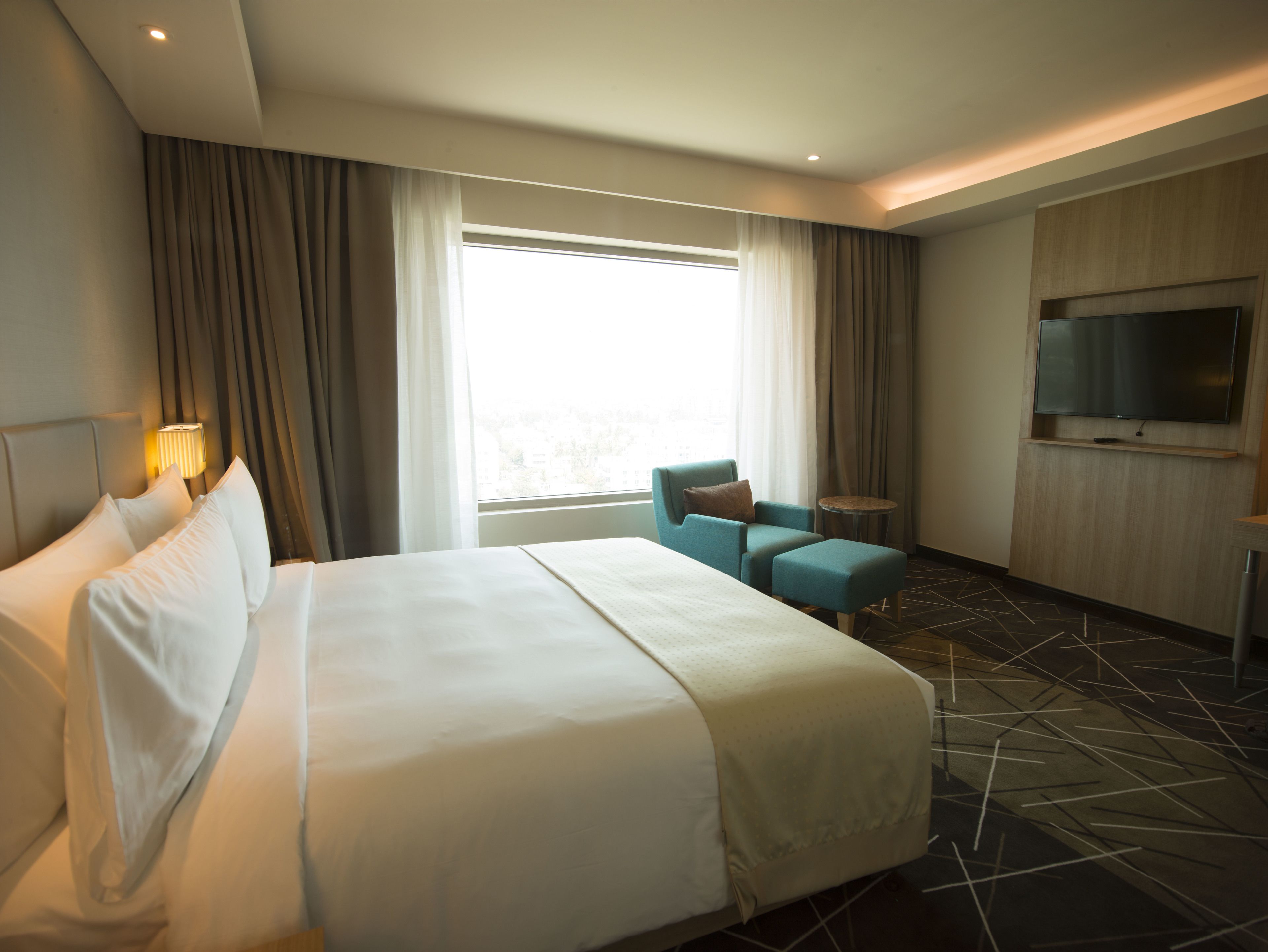 A hotel room with a large bed, a TV mounted on the wall, a small table, and a chair.