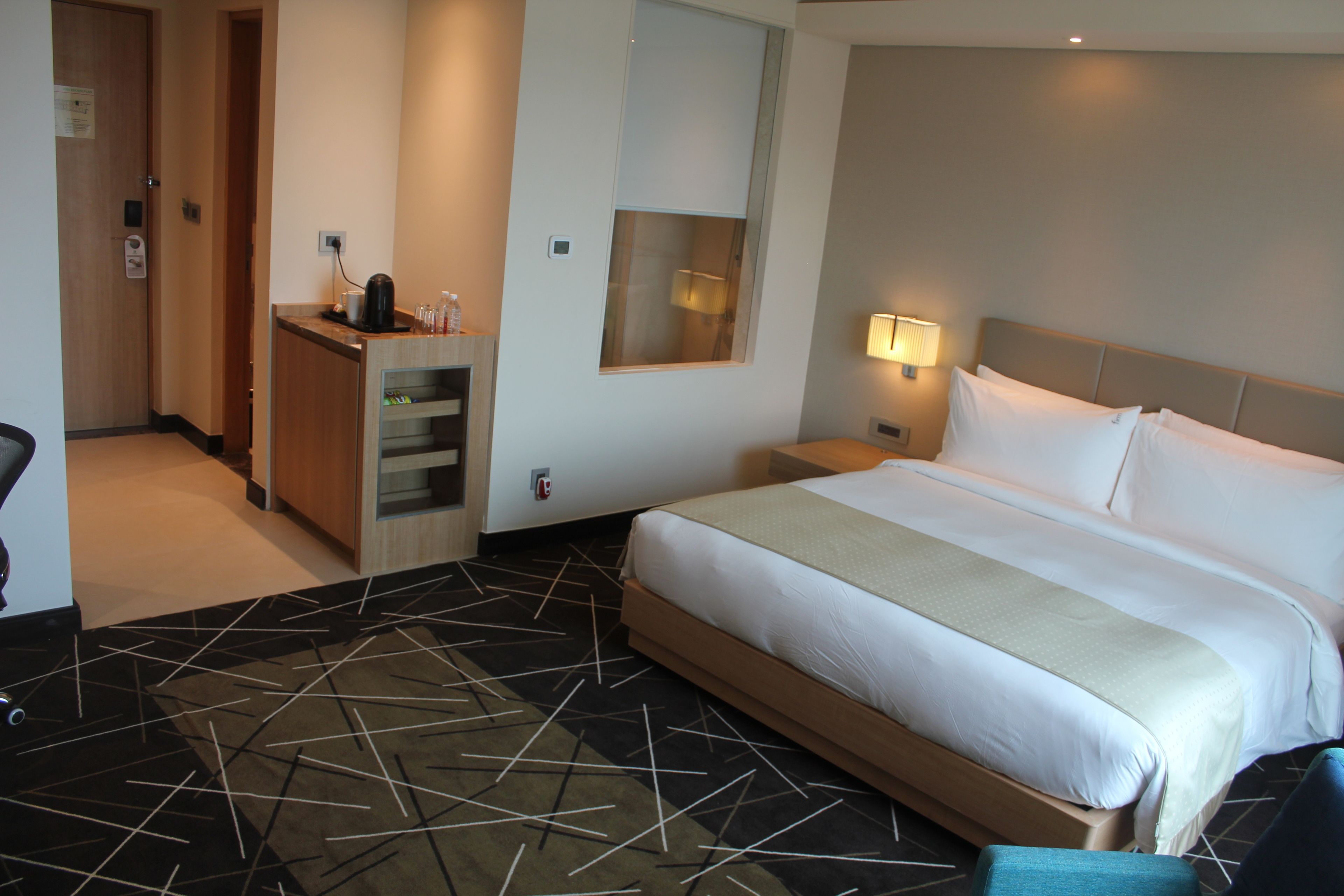 Une chambre d’hôtel avec un grand lit, un bureau avec une chaise, un miroir et une table de chevet avec une lampe.