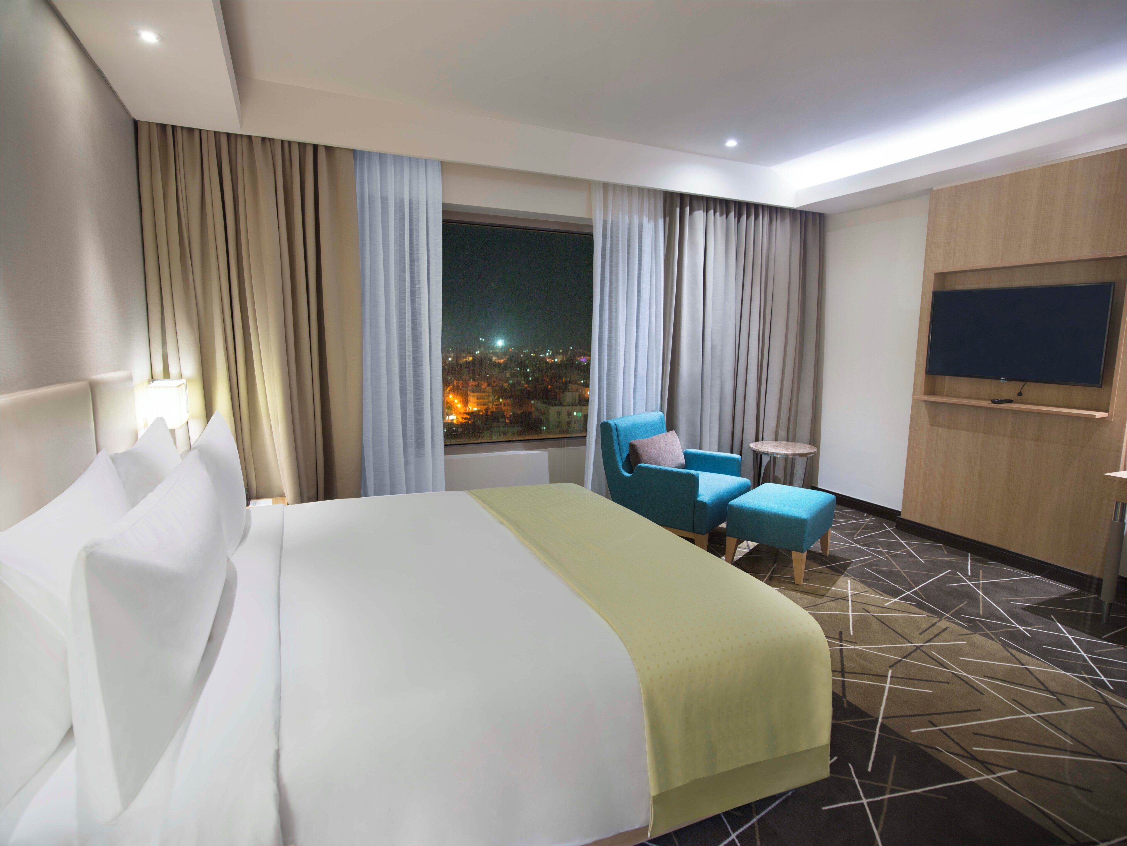A hotel room with a large bed, a chair, a small table, and a TV mounted on the wall.