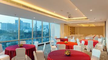 A conference room with round tables, white chairs, and red tablecloths. Large windows offer a city view.