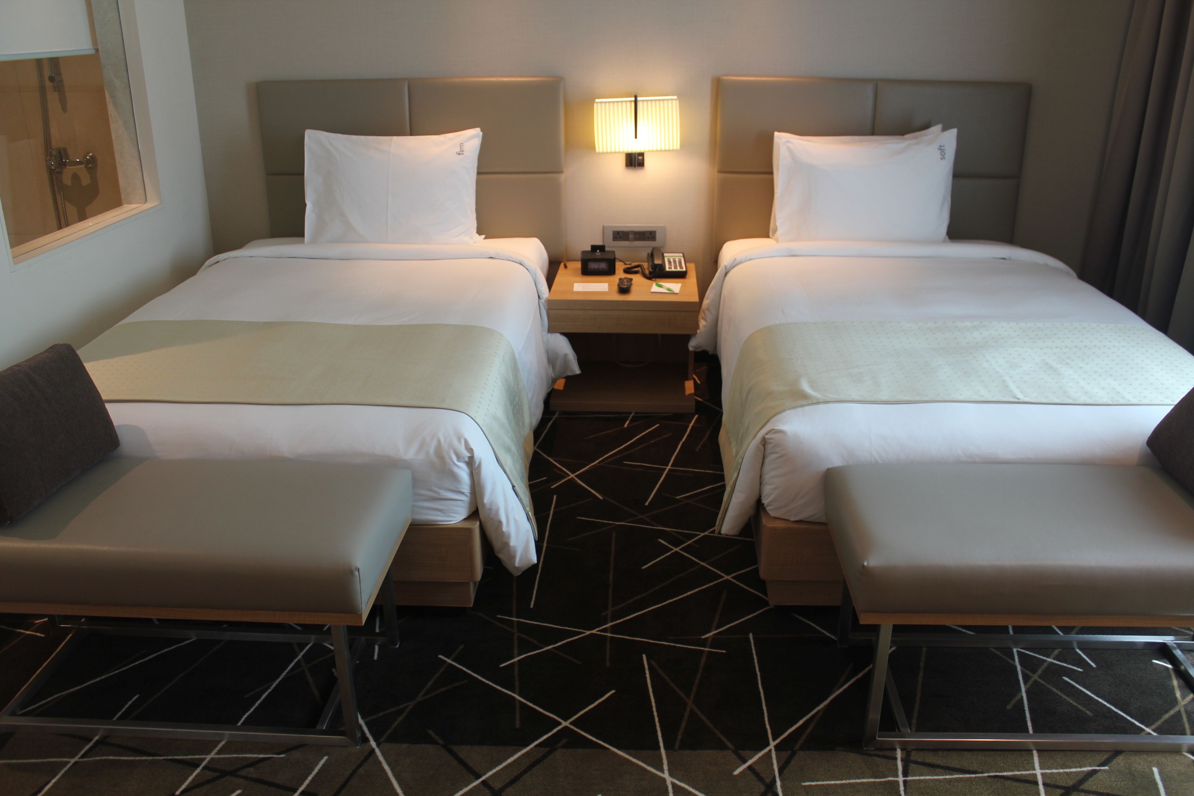 A hotel room with two beds, a nightstand, a lamp, and a modern geometric-patterned carpet.