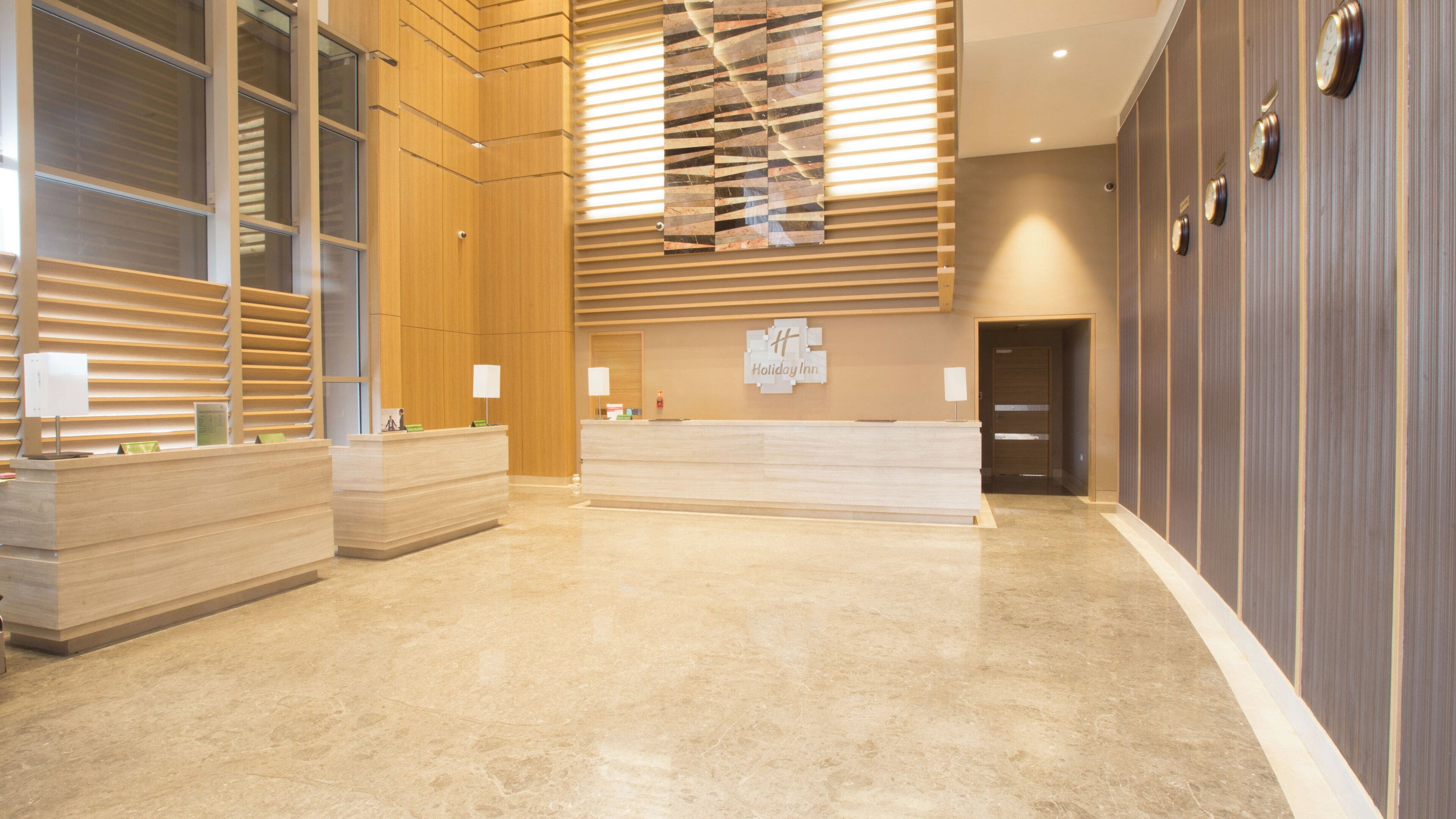 A hotel reception area with a reception desk, a clock, and a Holiday Inn sign.