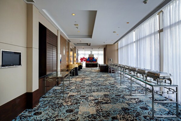 A hotel corridor with a patterned carpet, a long reception desk, and a television mounted on the wall.