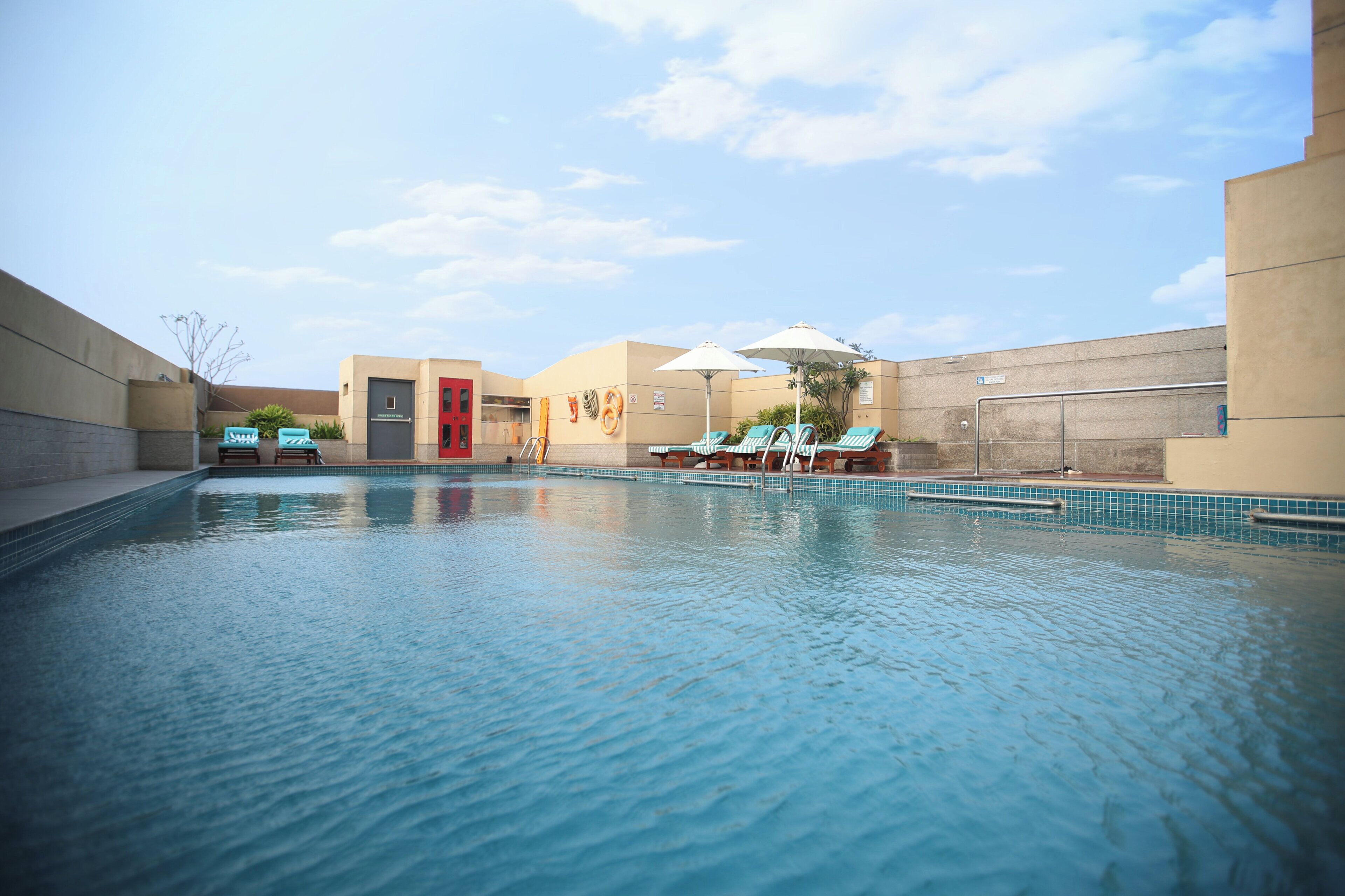 A swimming pool with lounge chairs and umbrellas, a red door, and a clear sky.