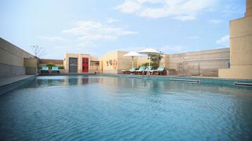 A swimming pool with lounge chairs and umbrellas, a red door, and a clear sky.