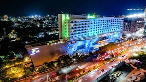 Un hotel de varios pisos con un letrero llamativo, rodeado de una calle urbana con mucho movimiento al caer la noche.