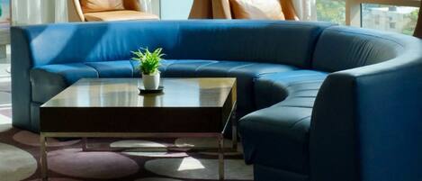Una sala de estar moderna con un sofá seccional azul, dos sillones de cuero, una mesa de centro y dos lámparas colgantes de malla negra.