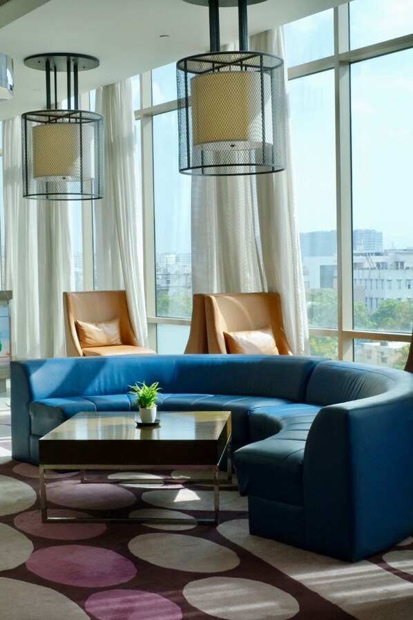Un salon moderne avec un canapé d’angle bleu, deux fauteuils en cuir, une table basse et deux suspensions noires en treillis métallique.