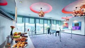 A spacious room with a long table set for a buffet, large windows, and modern ceiling lights. - Leonardo Hotel Munich City South (Munich)