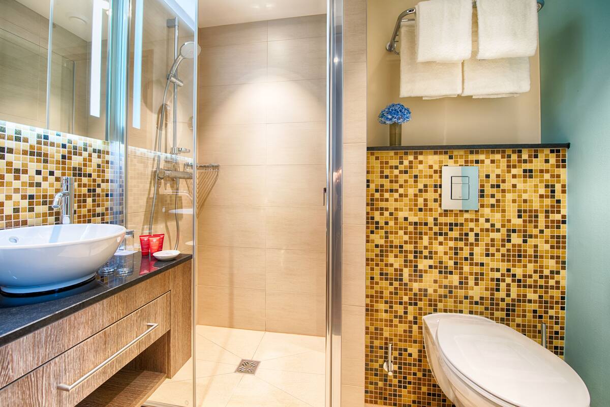 Un baño moderno con ducha envuelta en vidrio, un lavamanos grande y blanco, y una pared con mosaicos.