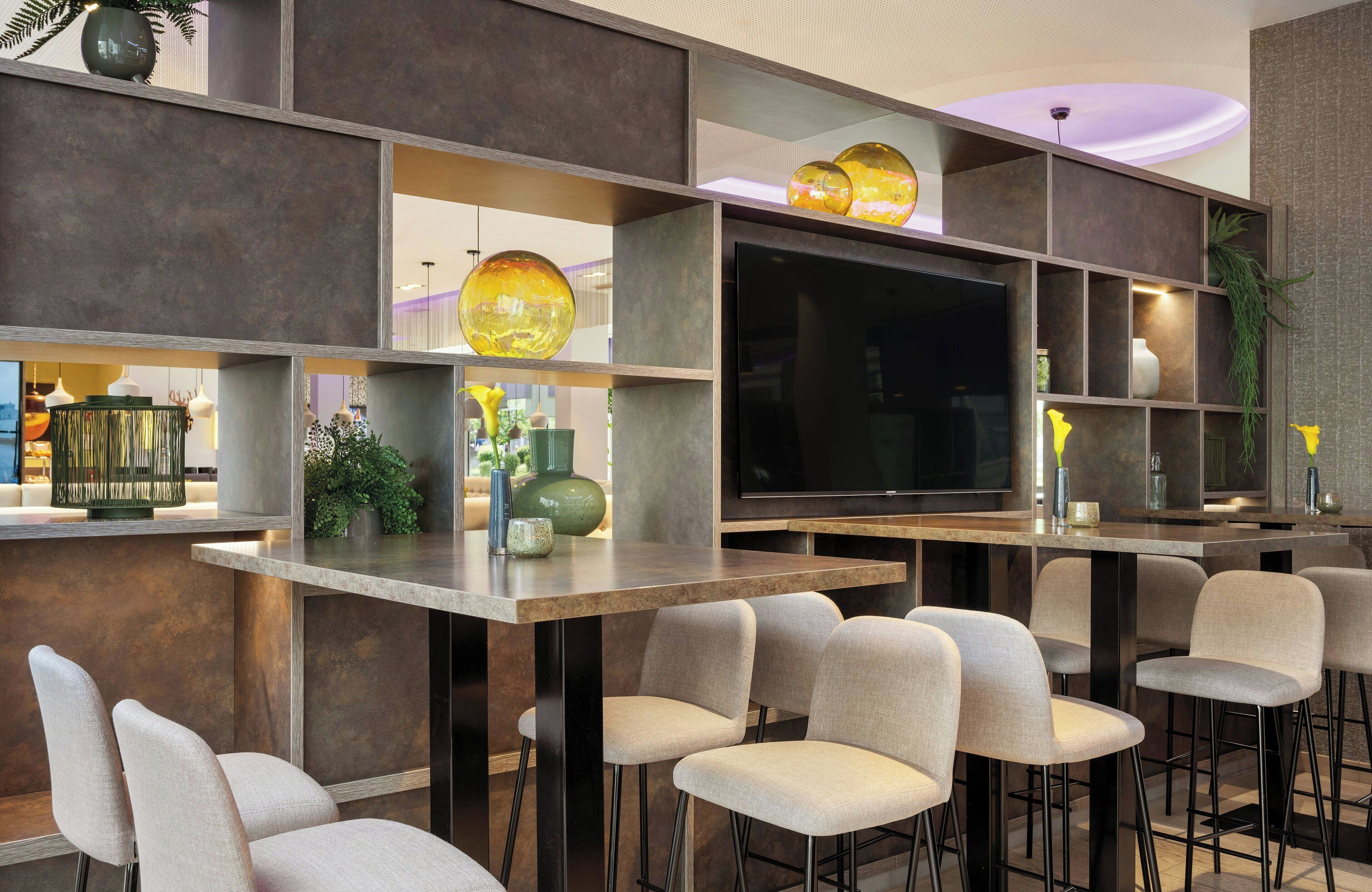 Zona de bar moderna con televisión de pantalla plana, taburetes y iluminación decorativa.